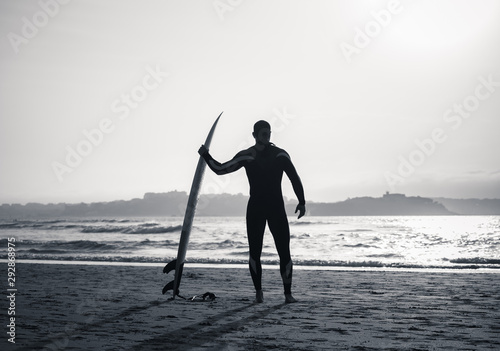 Silhouette of surf man standing with surfboard looking at ocean ready for the high waves.