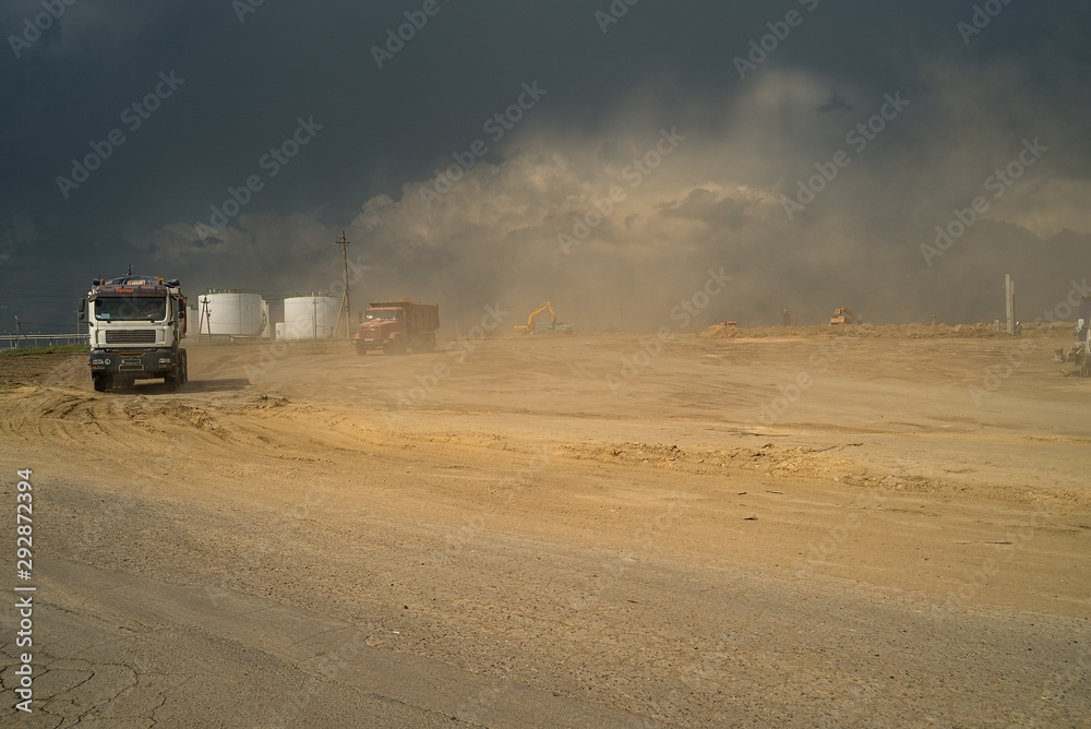  This is a large construction site from which trucks transport ground, against the backdrop of gloomy clouds