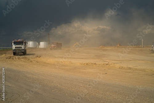  This is a large construction site from which trucks transport ground, against the backdrop of gloomy clouds