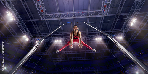 Male athlete doing a complicated exciting trick on gymnastics rings in a professional gym. Man perform stunt in bright sports clothes photo