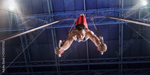 Male athlete doing a complicated exciting trick on gymnastics rings in a professional gym. Man perform stunt in bright sports clothes photo
