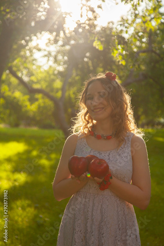 Young woman in white cute polka dot dress walking in an apple garden on a lovely sunny summer day