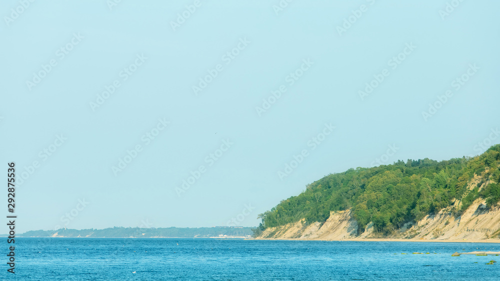the picturesque landscape of the steep wooded shore of the blue sea under a clear sunny sky