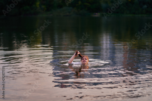 The girl in the shirt bathes in the river holds her hair