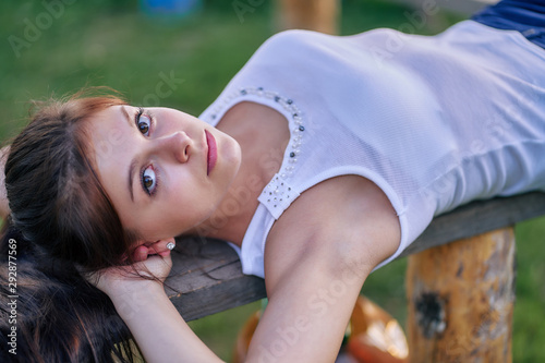 A beautiful young girl is lying on a bench, she is looking at the camera. Girl with her hair in a white T-shirt