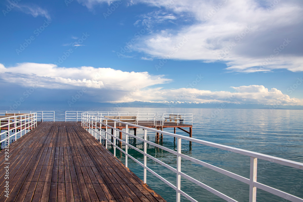 Pier on Issyk-Kul Lake on the background of a mountain range with snowy peaks and cloudy sky