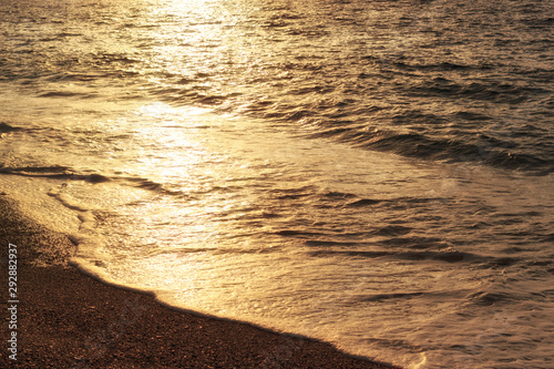 Sunset reflection on sea waves. Golden sunlight on waves of coastline. Sea beach at evening  summer vacation.