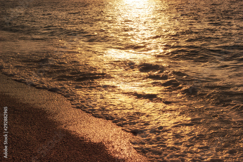 Golden sunlight on waves of coastline. Sea beach at evening, summer vacation. Sunset reflection on sea waves.