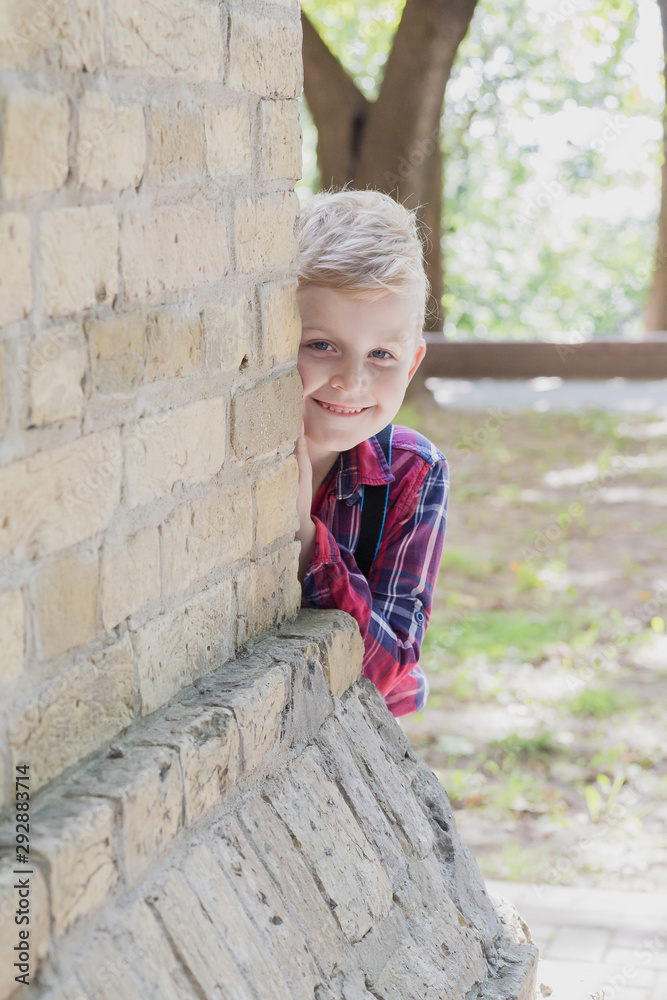 Little boy peeks out from behind a wall in a park. Little boy peeks out from behind a wall in a park.