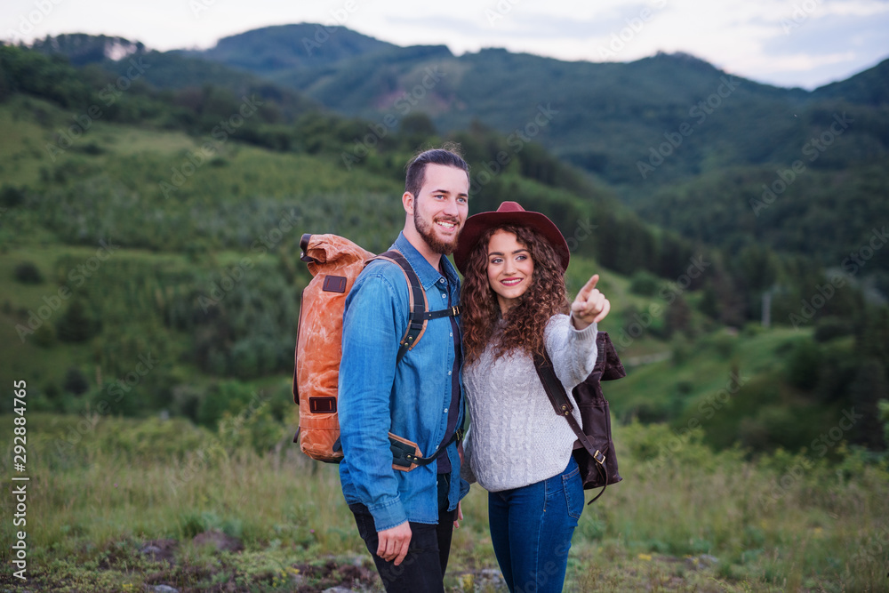 Young tourist couple travellers with backpacks hiking in nature, talking.