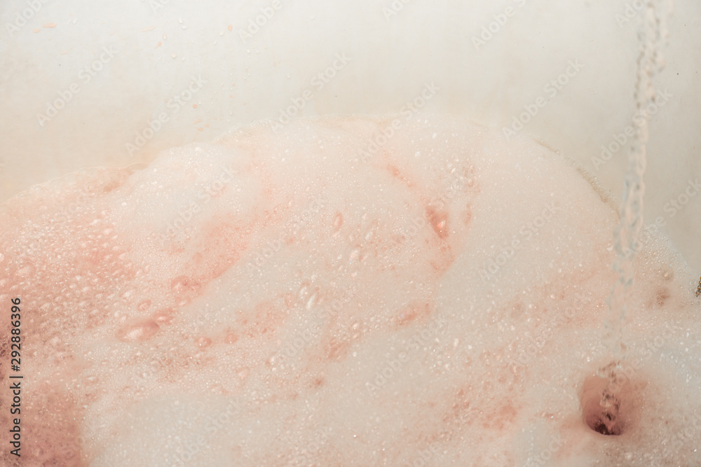 Fototapeta premium Soapy foam painted red with a pouring stream of water is close