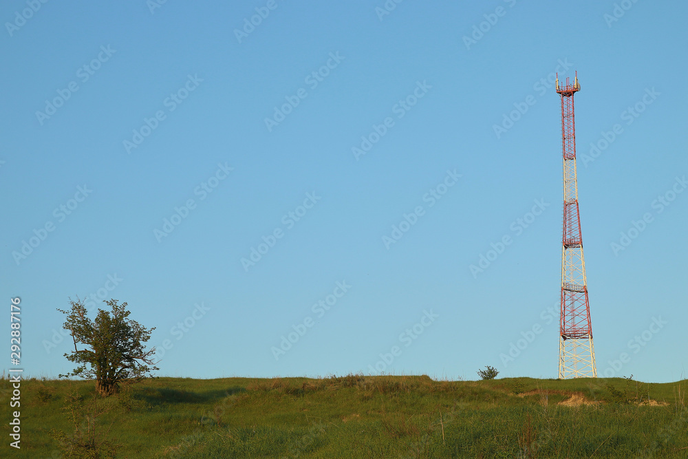 Obraz premium Communications tower at the blue sky background and green meadow