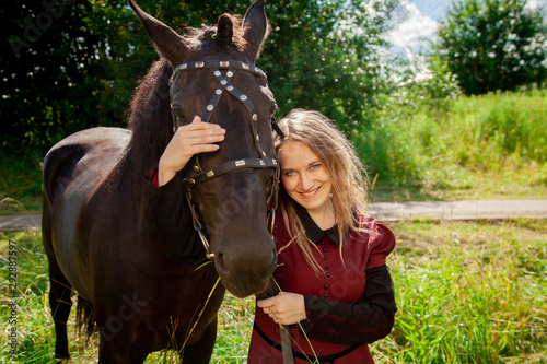 Beautiful caucasian young girl walking with a horse and enjoys summertime in countryside. © goldeneden