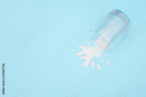 Spilled milk. Overturned glass with milk on blue background. Dairy abandonment concept Copy space Top view photo