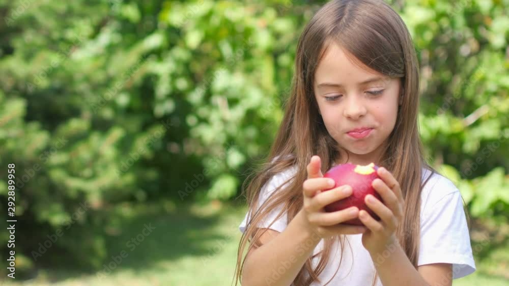 Cute little girl bites and eats a fresh red apple. Chews and smiles. Healthy tasty food concept. Cute little girl bites and eats a fresh red apple. Chews and smiles. Healthy tasty food concept.