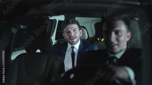 Two men drive in car and talk.