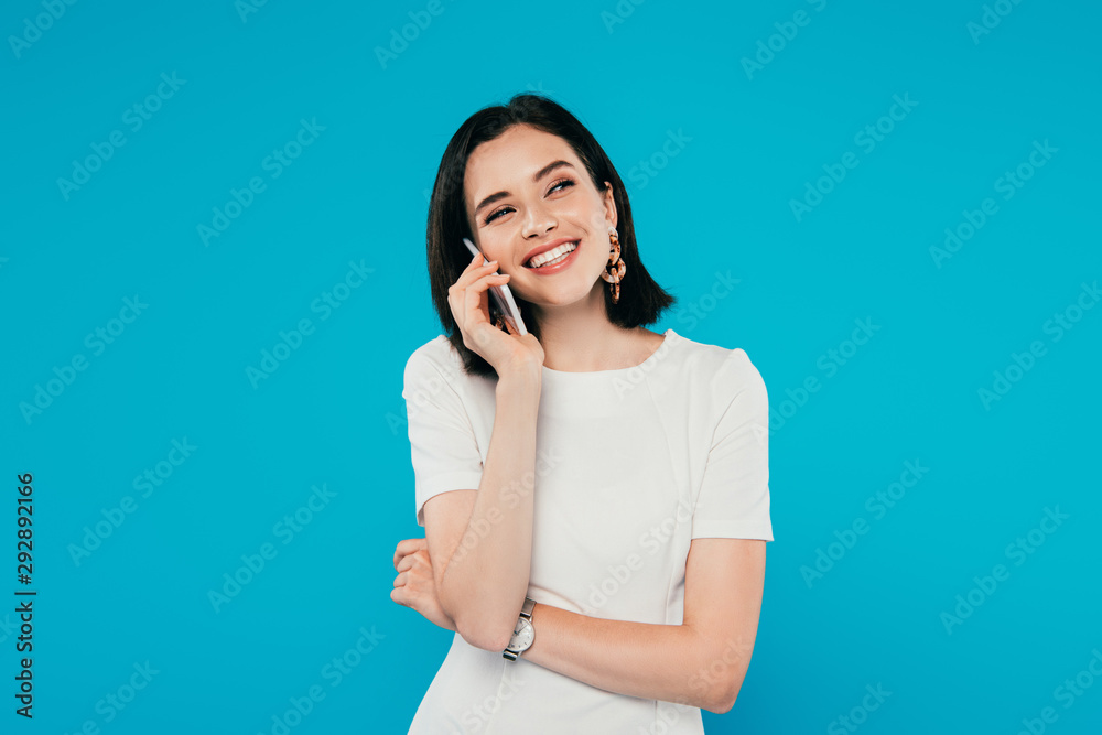 smiling elegant woman in dress talking on smartphone and looking away isolated on blue smiling elegant woman in dress talking on smartphone and looking away isolated on blue