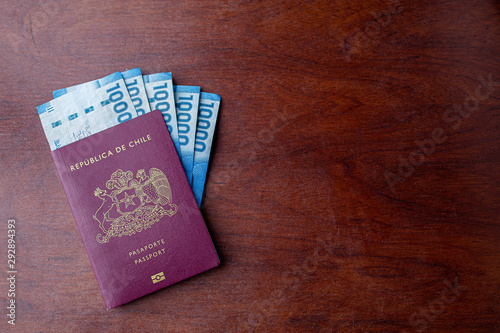 One Red Chilean passport with  and some Pesos Chilenos on a wooden desk