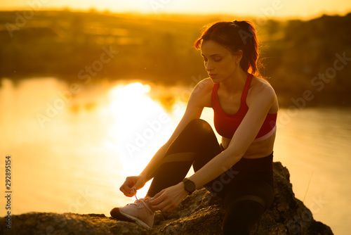 Young Sports Woman Tying Running Shoes and Preparing for Trail Run at Sunset. Healthy Lifestyle and Sport Concept.