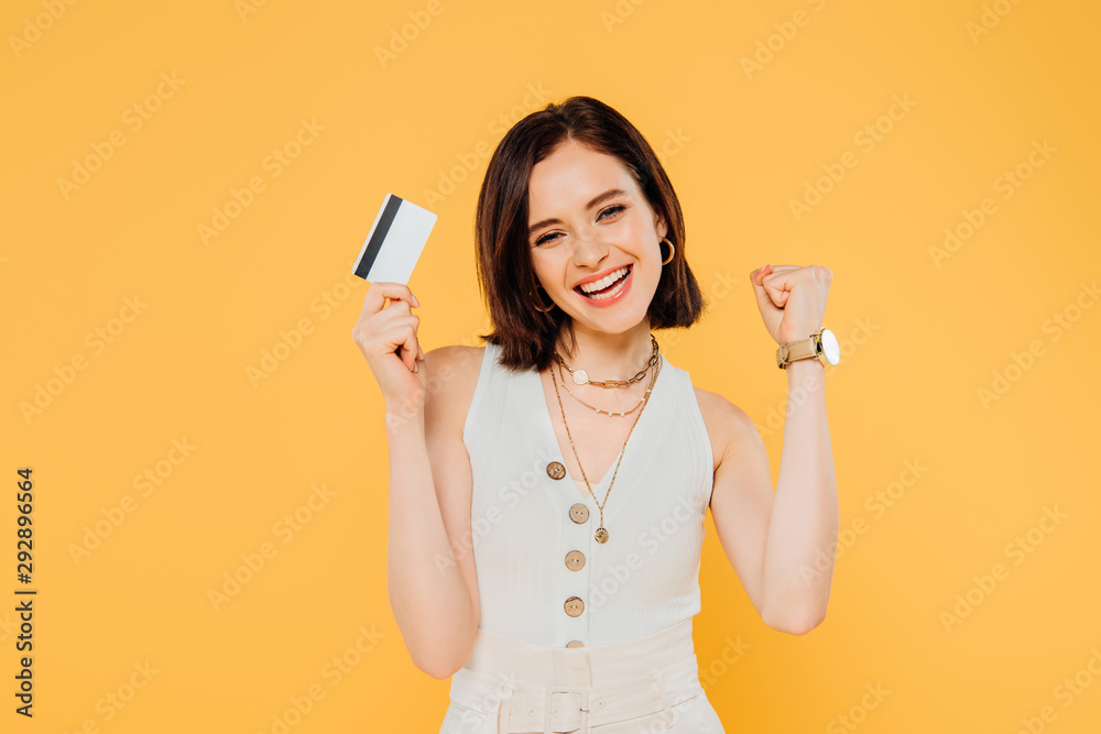 happy elegant girl holding credit card and showing yes gesture isolated on yellow happy elegant girl holding credit card and showing yes gesture isolated on yellow