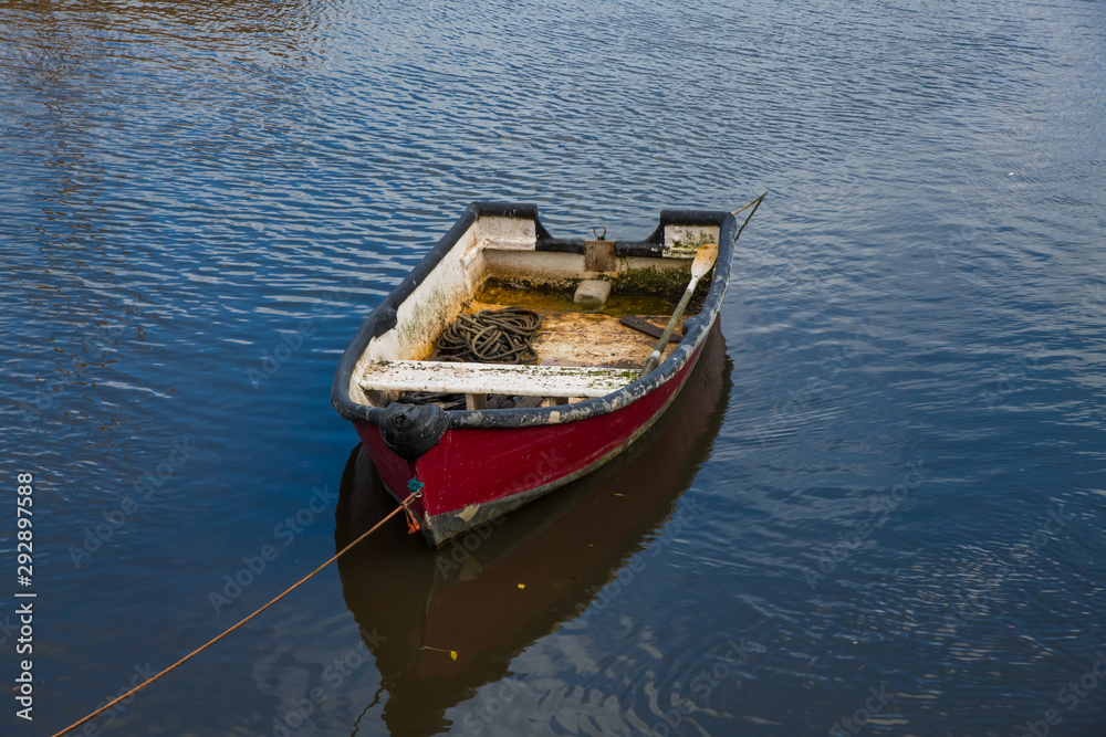 A worn red wooden rowing boat in a harbour