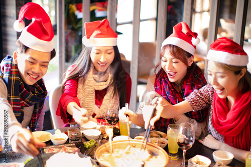 Happy friends having fun and celebrating christmas in hot pot restaurant