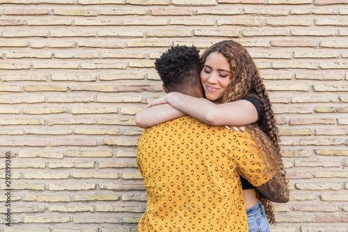 interracial couple hugging on a brick wall