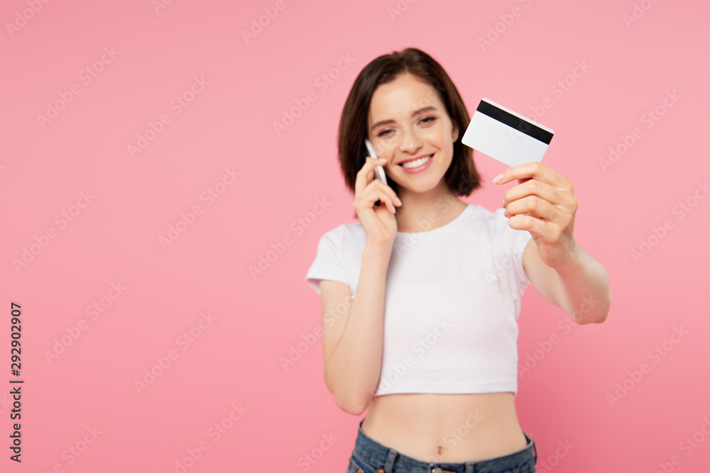 smiling girl holding credit card and talking on smartphone isolated on pink smiling girl holding credit card and talking on smartphone isolated on pink