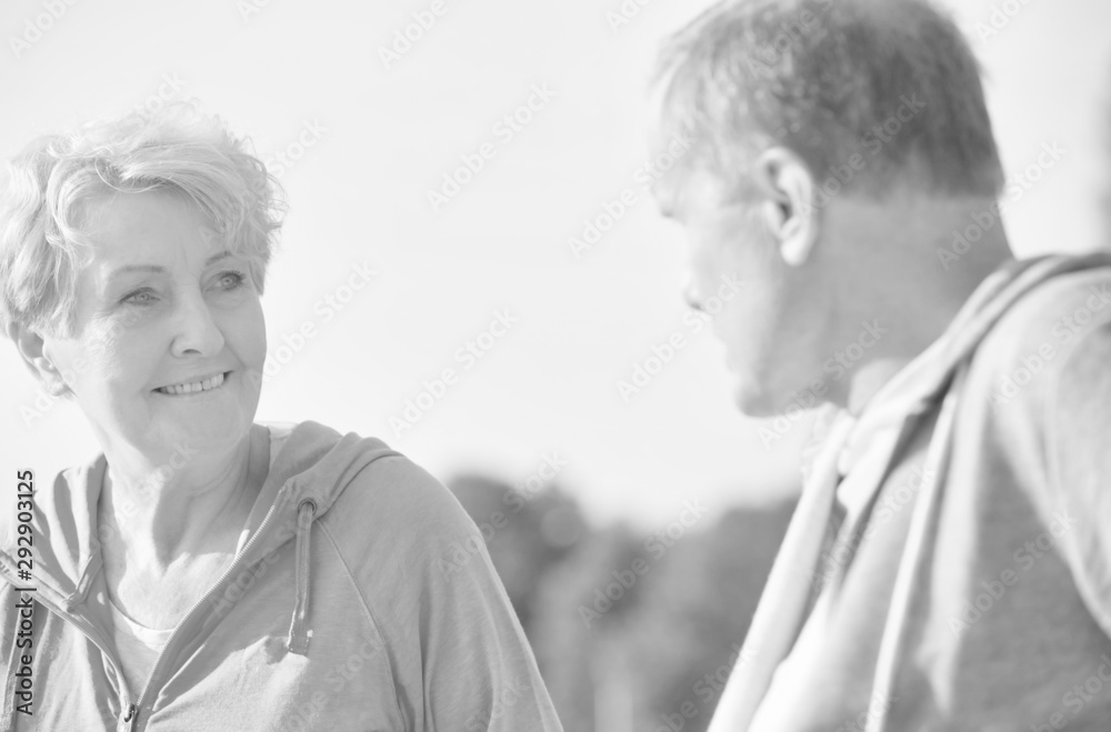 Black and white photo of Active senior couple talking while resting on bench at park Black and white photo of Active senior couple talking while resting on bench at park