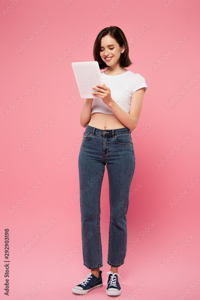full length view of beautiful smiling girl using digital tablet isolated on pink full length view of beautiful smiling girl using digital tablet isolated on pink