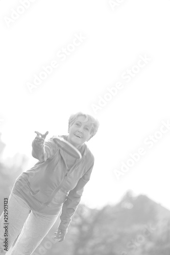 Black and white photo of Smiling and healthy senior woman throwing disc in park