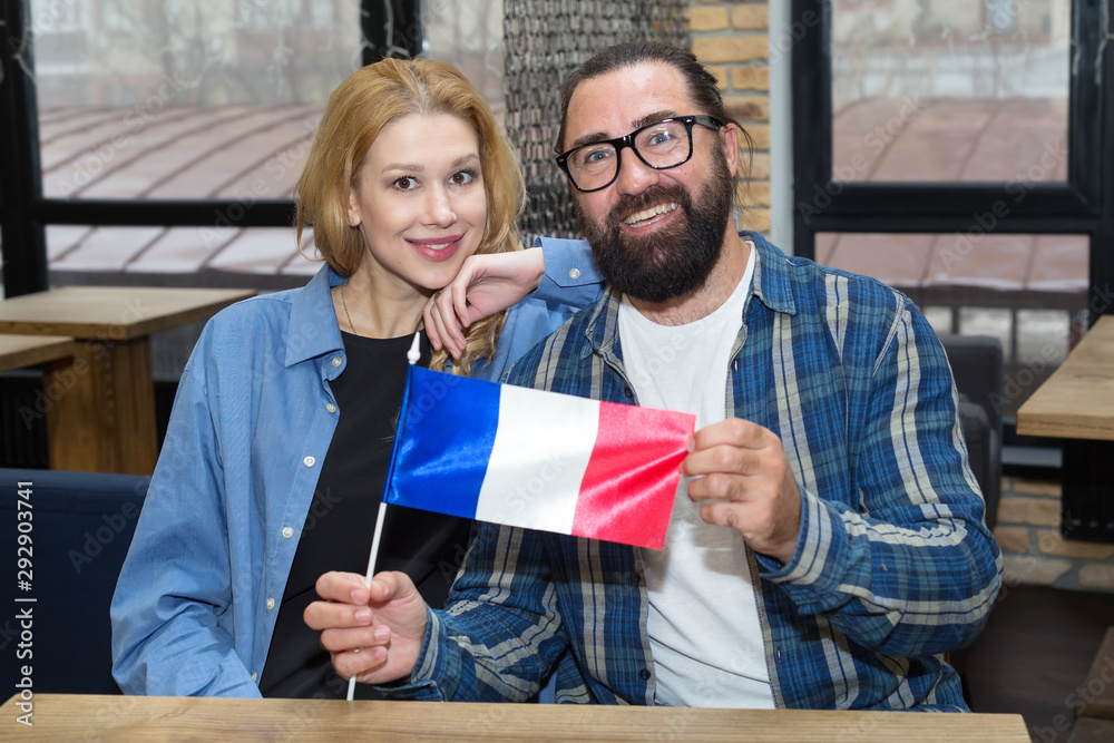 Couple, bearded man in glasses and blond woman with France flag sitting in office.