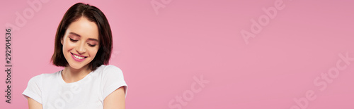 Slika na platnu panoramic shot of beautiful smiling shy girl looking down isolated on pink