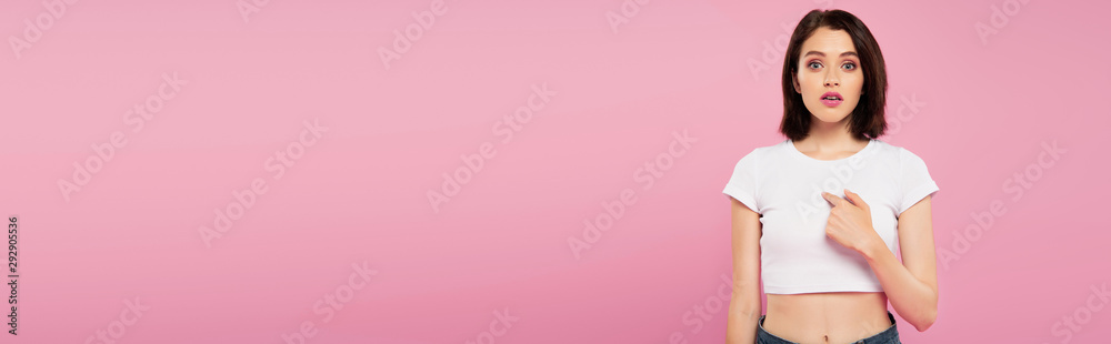 panoramic shot of beautiful surprised girl pointing with finger at herself isolated on pink