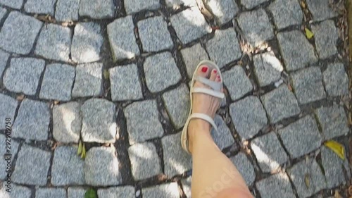 female legs in grey sandals walk along a cobblestone pavemen, first-person view, 4k photo