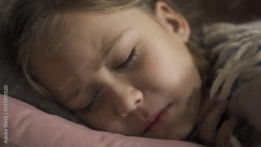 Close-up face of sick caucasian girl coughing while lying under blanket at home. The sad child has fever. Concept of health, illness, sickness, common cold, treatment Close-up face of sick caucasian girl coughing while lying under blanket at home. The sad child has fever. Concept of health, illness, sickness, common cold, treatment