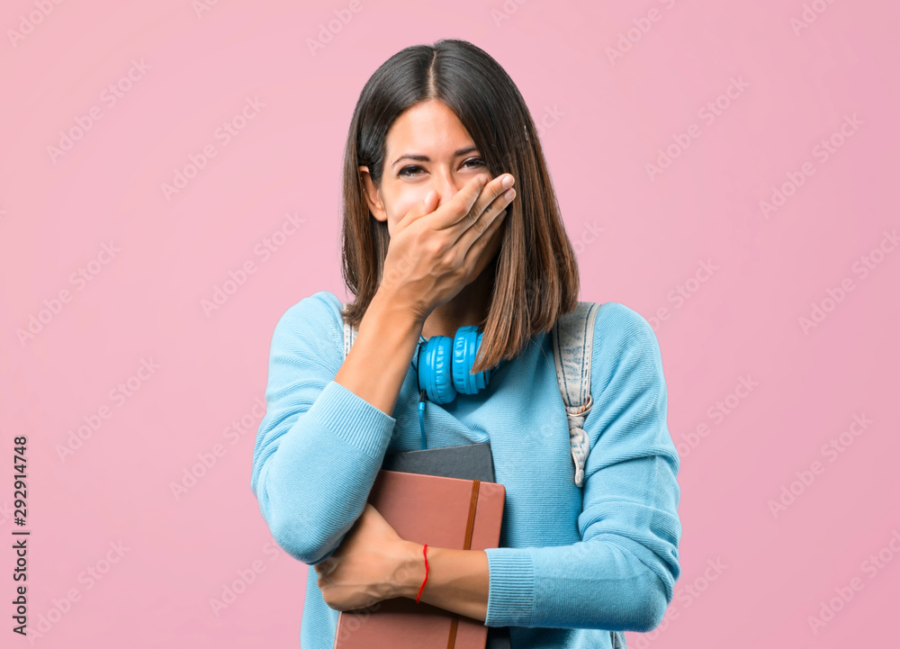 Young student girl with blue sweater and headphones smiling a lot while covering mouth on pink background Young student girl with blue sweater and headphones smiling a lot while covering mouth on pink background