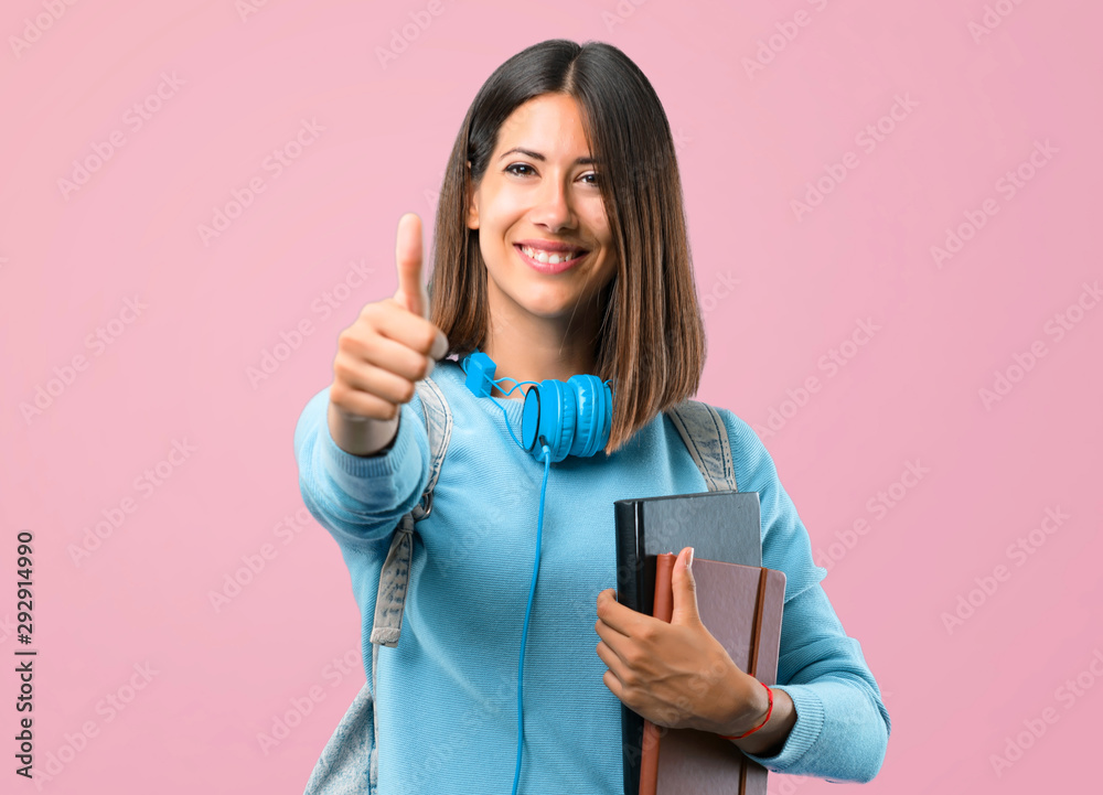 Young student girl with blue sweater and headphones giving a thumbs up gesture and smiling because something good has happened on pink background Young student girl with blue sweater and headphones giving a thumbs up gesture and smiling because something good has happened on pink background