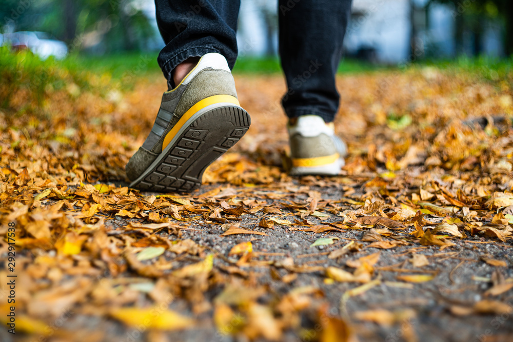 Walk on pavement in Autumn. Back view on the feet of a man walking along the pavement with fallen foilage. Abstract empty blank Autumn weather background Walk on pavement in Autumn. Back view on the feet of a man walking along the pavement with fallen foilage. Abstract empty blank Autumn weather background