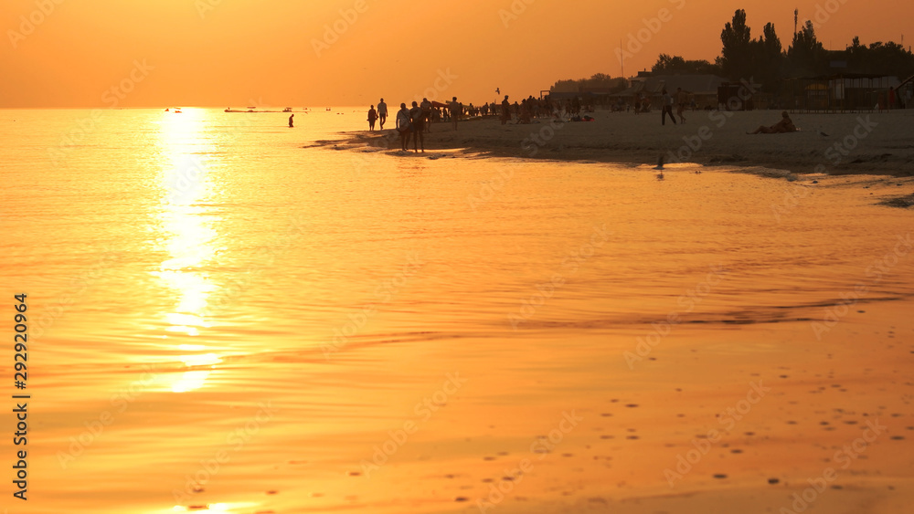 People walking on beach at sunset. Magic orange sunset over sea. Picturesque evening scene.