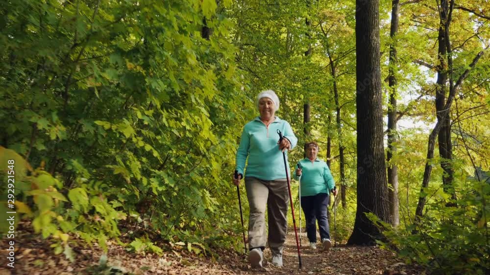 Nordic walking for elderly women outdoor - two senior ladies has training in autumn forest. Women happy and go at a fast pace Nordic walking for elderly women outdoor - two senior ladies has training in autumn forest. Women happy and go at a fast pace