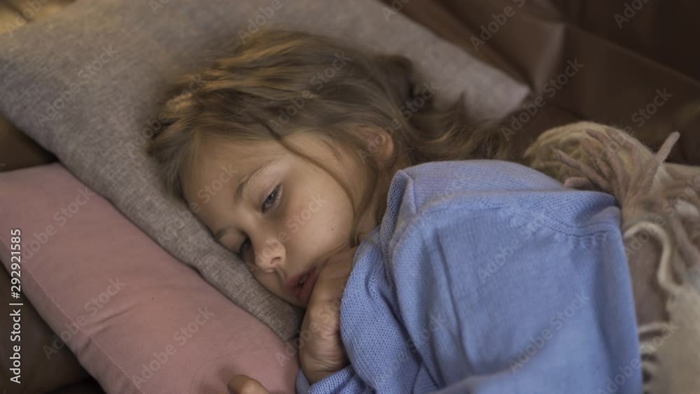 Young little girl in blue warm sweater taking temperature. Close-up of a a sad child laying at home with fever. Young little girl in blue warm sweater taking temperature. Close-up of a a sad child laying at home with fever.