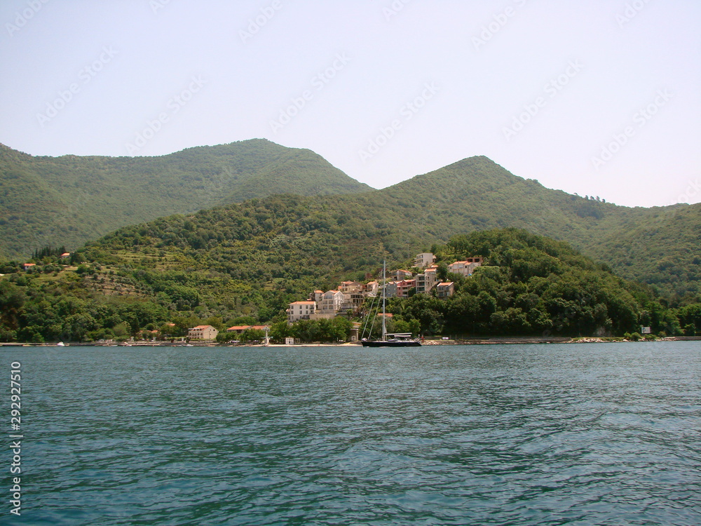 Landscape from the sea of ​​small Montenegrin seaside settlements near the azure bay surrounded by hills covered with dense green forest.