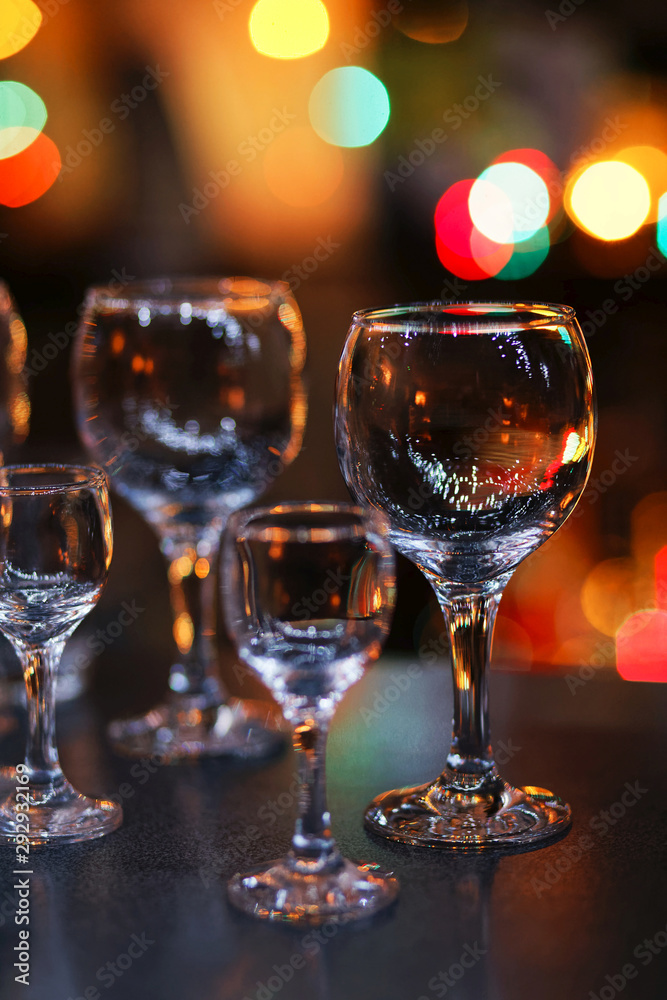 Empty glass transparent wine glasses on a table and colorful lights on a blurry dark background. Shallow focus. Empty glass transparent wine glasses on a table and colorful lights on a blurry dark background. Shallow focus.