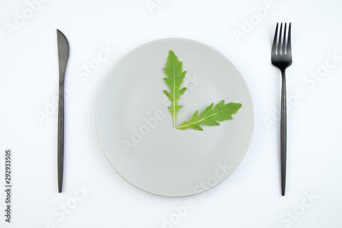 Arugula leaves on a gray plate in the form of hour hands. The concept of proper and dietary nutrition.