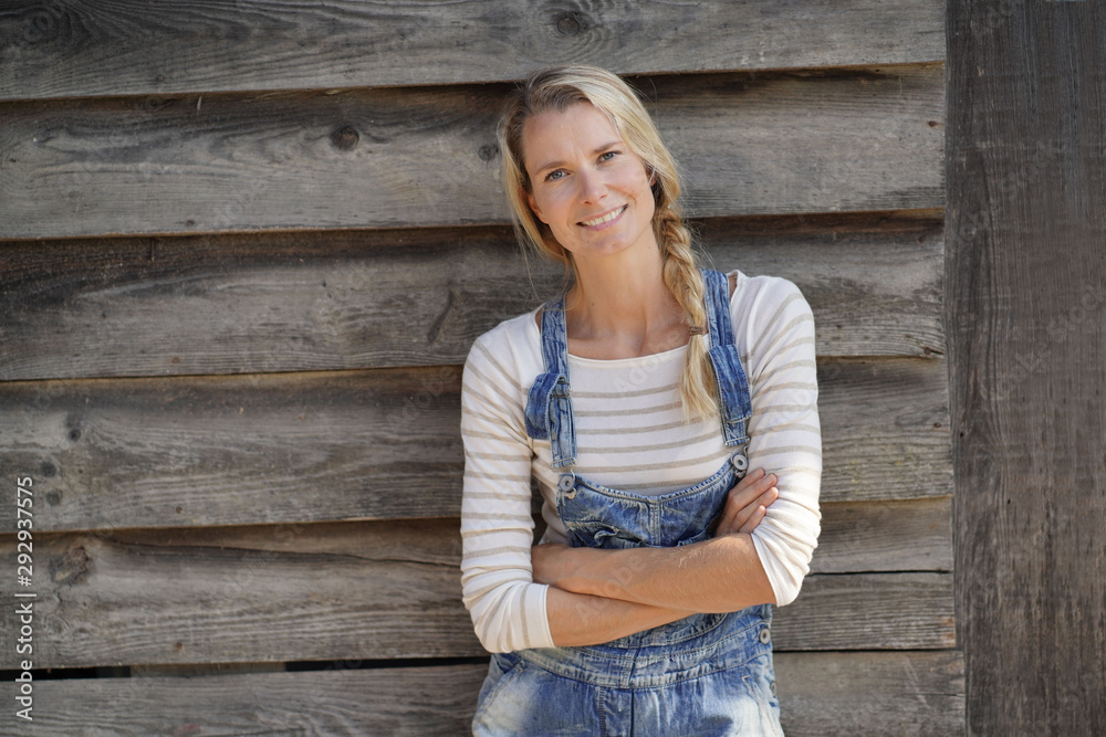 Smiling blond woman with overalls standing in front of barn Smiling blond woman with overalls standing in front of barn