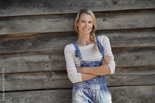 Smiling blond woman with overalls standing in front of barn photo