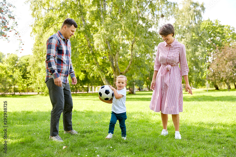 Fototapeta premium family, leisure and people concept - happy mother, father and little son with ball playing soccer at summer park