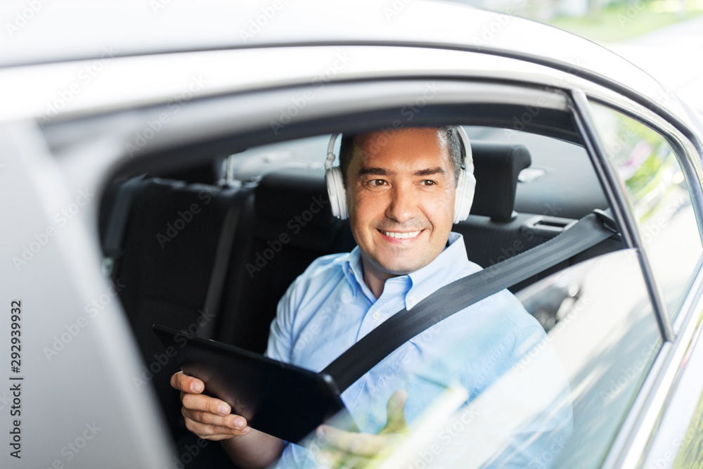 transport, business and technology concept - male passenger or businessman with wireless headphones using tablet pc computer on back seat of taxi car