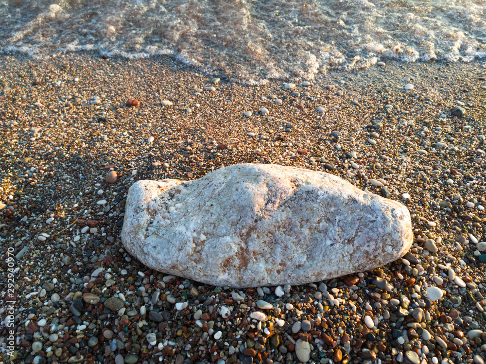 An oblong boulder on a beach by the sea. Side lighting reveals the texture of wet sand. An oblong boulder on a beach by the sea. Side lighting reveals the texture of wet sand.